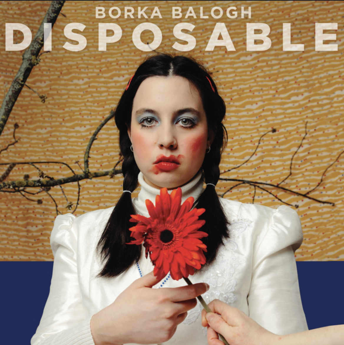 Studio portrait of a person in white holding a large red flower against a textured golden background.