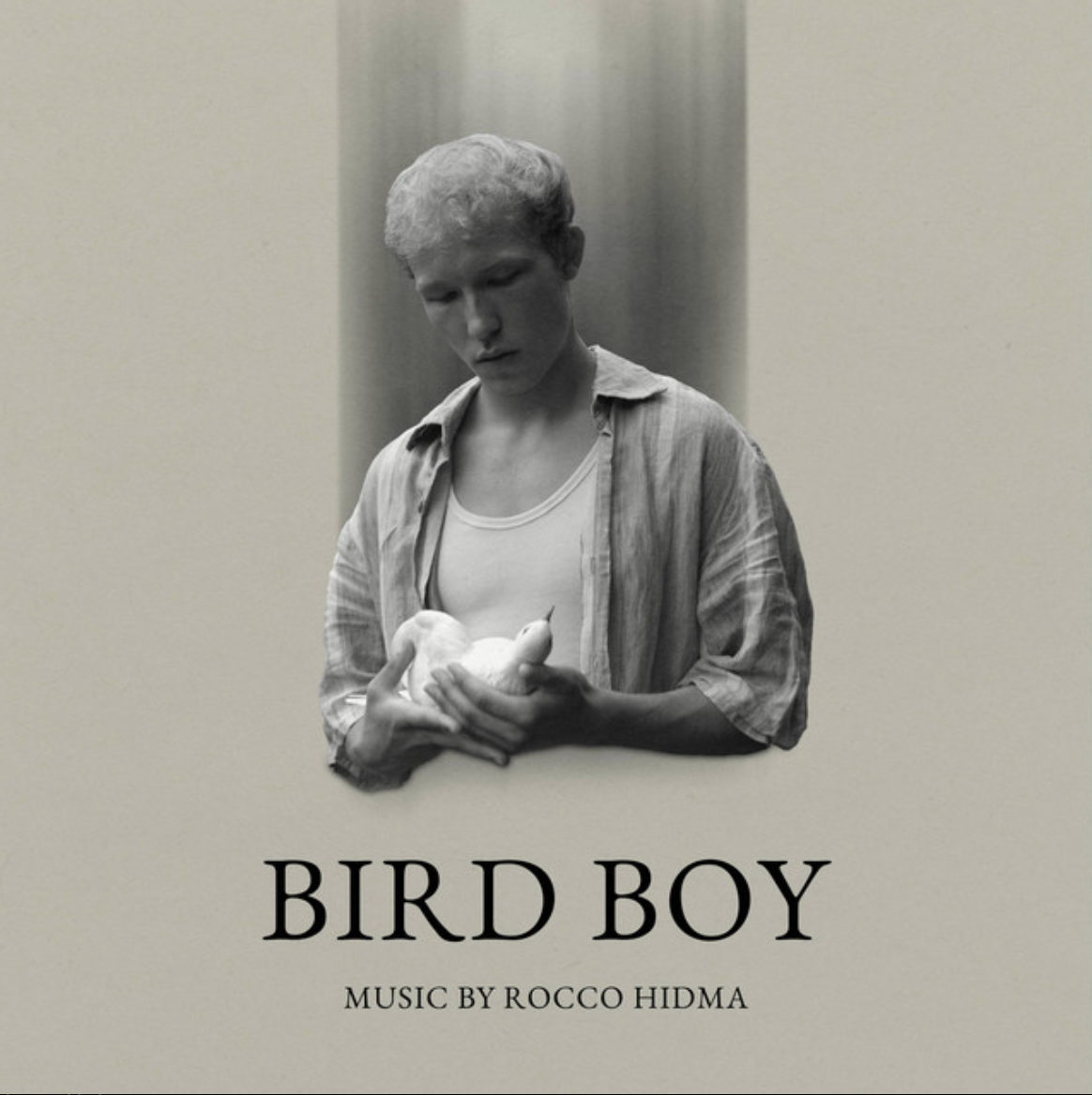 Black-and-white portrait of a young man holding a white bird against a minimalist background.