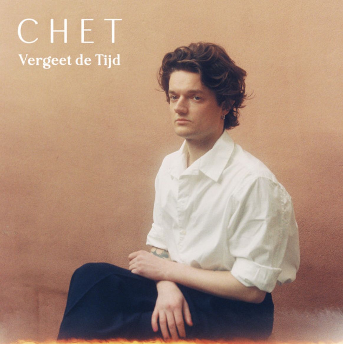 Warm-toned portrait of a seated young man wearing a white shirt against a neutral studio backdrop.