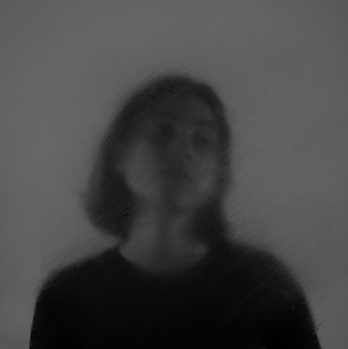 Soft-focus black-and-white portrait of a blurred person against a dark minimalist background.